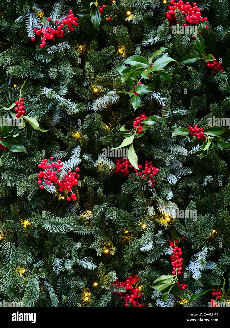 Weihnachtsdekoration mit grünen Kiefernblättern, roten Beeren und Lichtern, die Ende November 2019 in London, Großbritannien, zu sehen waren. Stockfoto