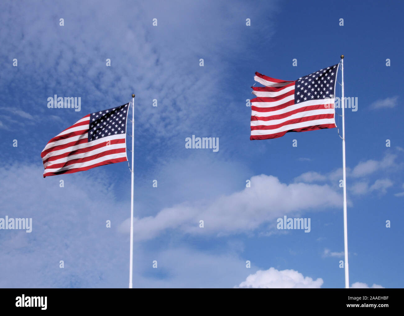 Zwei amerikanische Fahnen wehen im Wind gegen einen blauen Himmel mit dünnen Wolken. Stockfoto