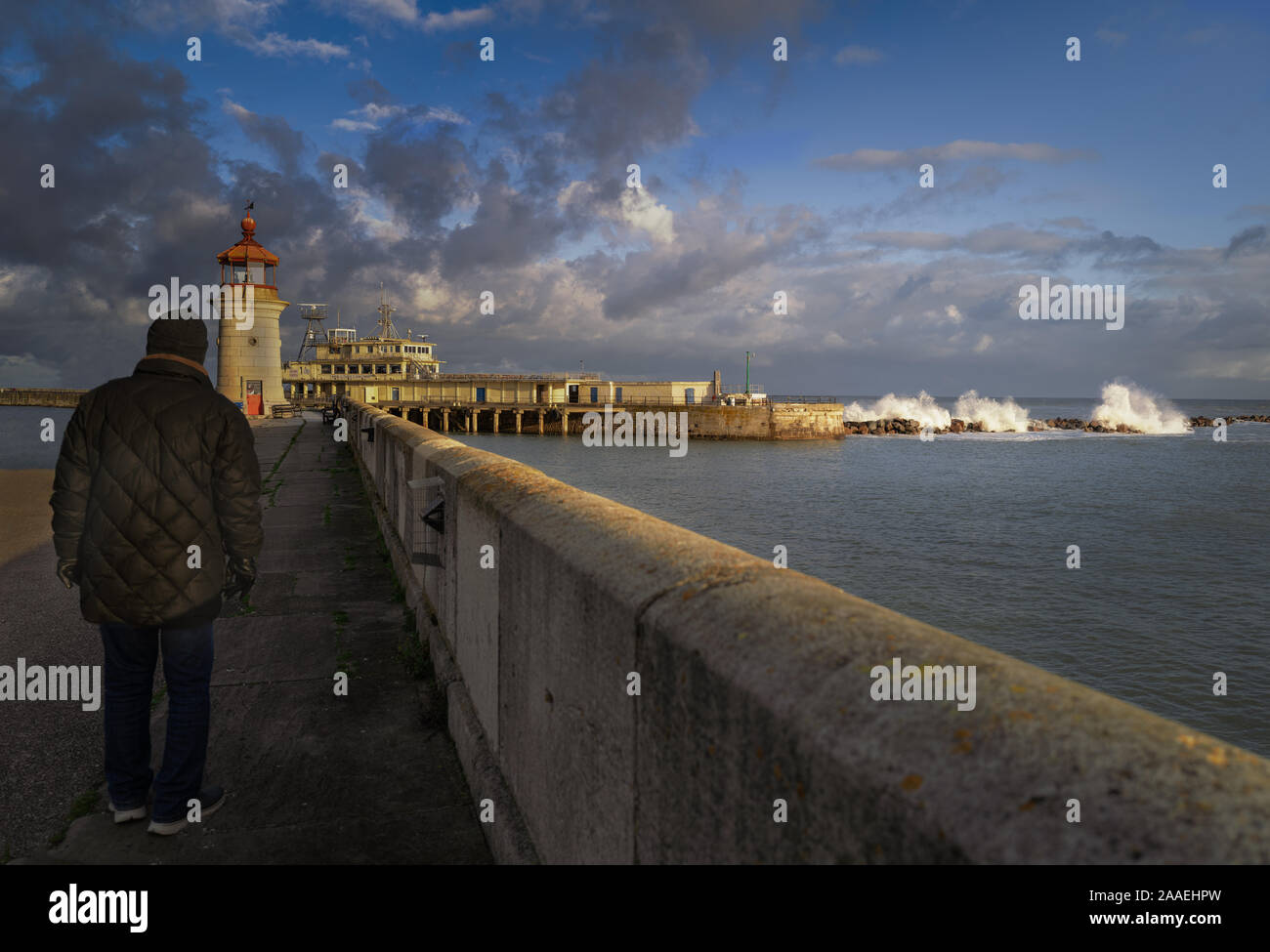 Ramsgate, England - Nov 18 Sonnenlicht verfängt sich die Wellen über die hafenmauer in Ramsgate Royal Harbour brechen als lokaler Mann Spaziergänge in Richtung der Leucht Stockfoto