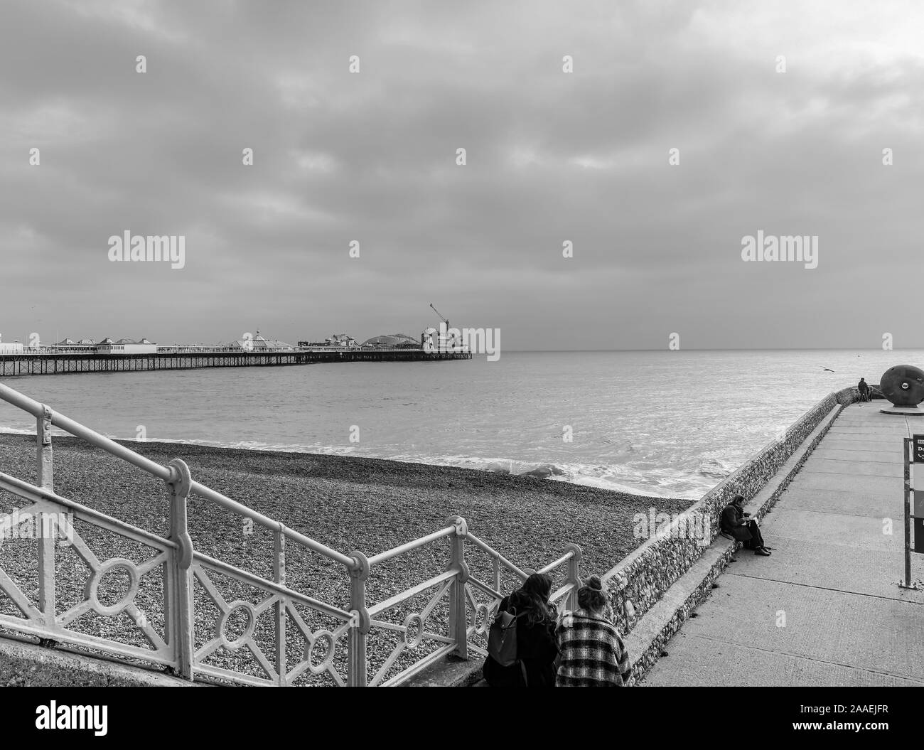 Kleine Pier in Brighton direkt am Kiesstrand. Der berühmte Pier im Hintergrund und einem dunklen Himmel ist Overhead. Stockfoto