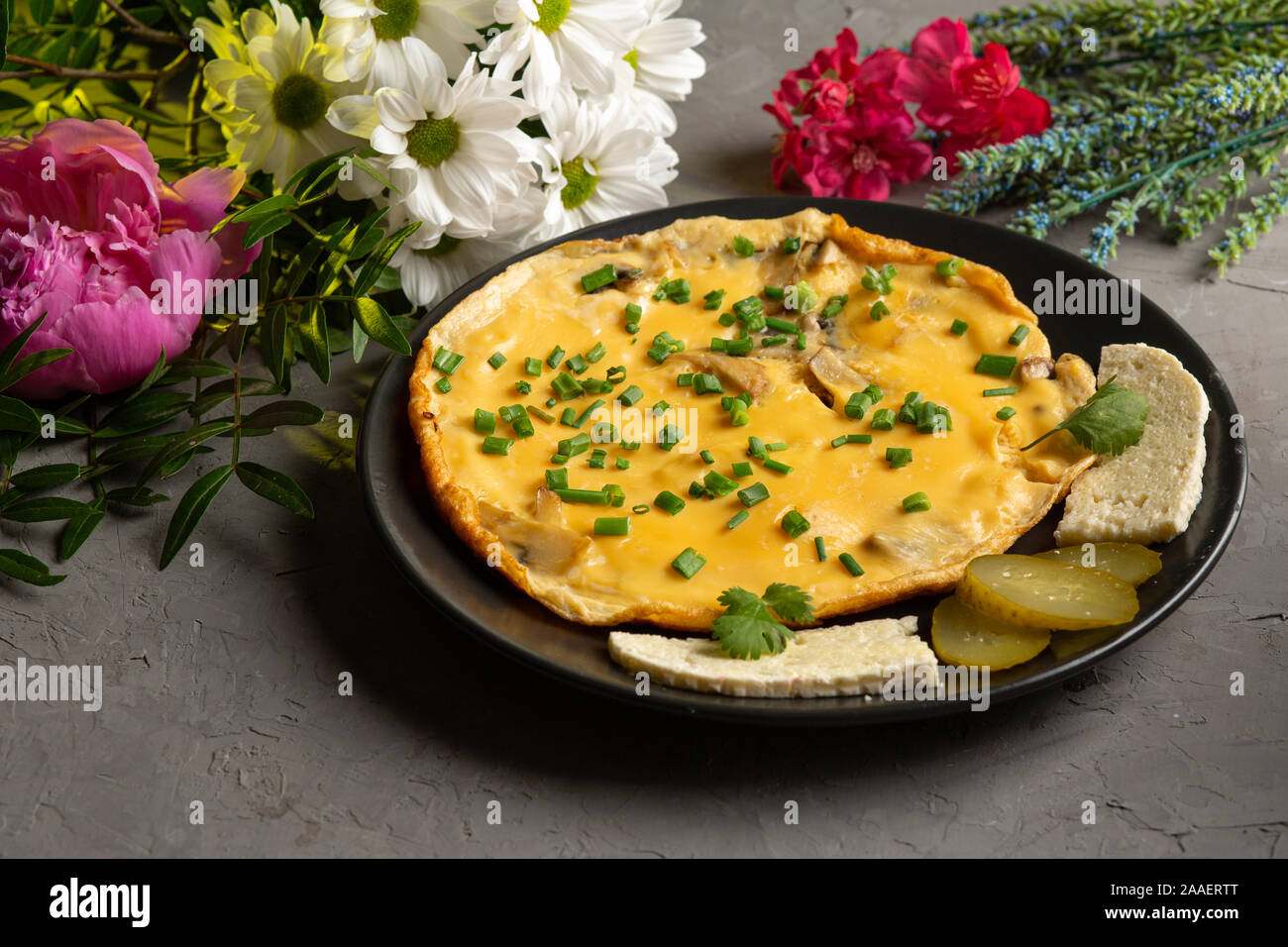 Omelette mit Pilzen und Kräutern mit Käse und Pickles in einer schwarzen Platte auf grauem Hintergrund Stockfoto