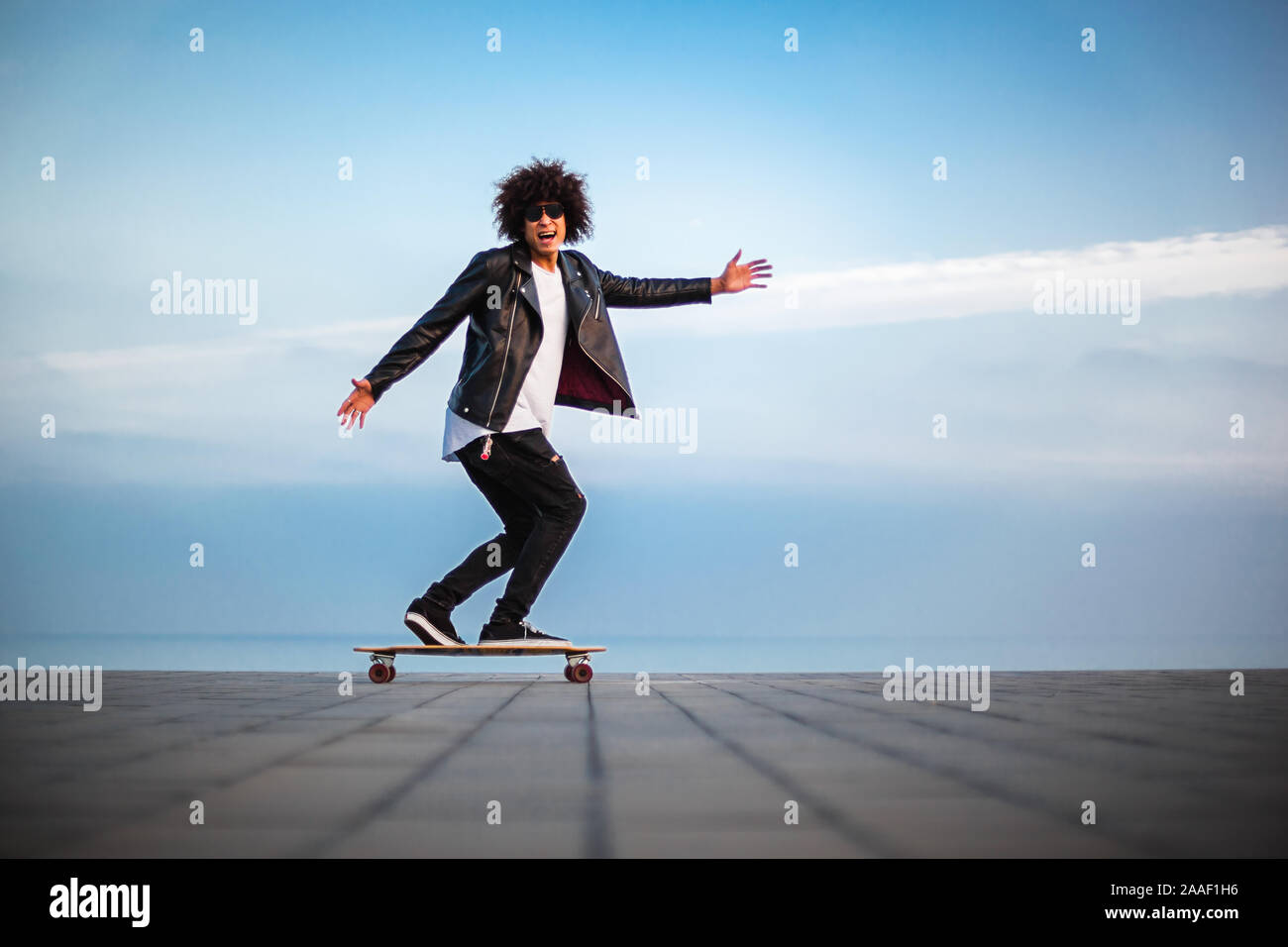 Hübscher junger afro-amerikanische Kerl mit Skateboard mit blauer Himmel, kopieren Raum Stockfoto