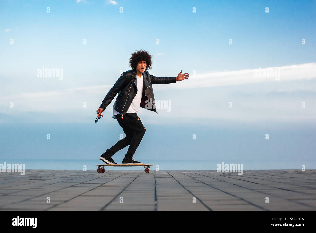 Hübscher junger afro-amerikanische Kerl mit Skateboard mit blauer Himmel, kopieren Raum Stockfoto