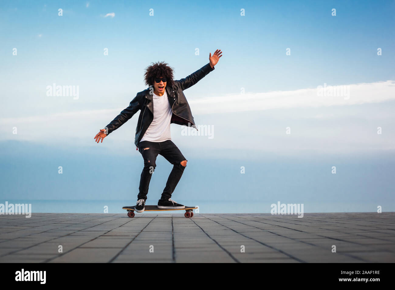 Hübscher junger afro-amerikanische Kerl mit Skateboard mit blauer Himmel, kopieren Raum Stockfoto
