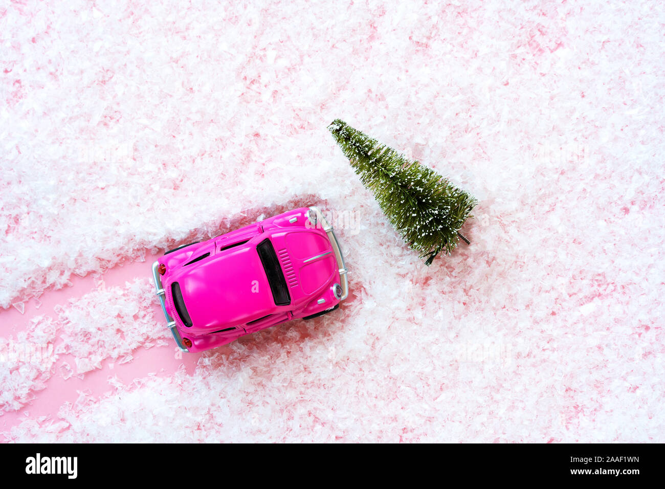 Kleines Spielzeug Kinder Auto und grünen Weihnachtsbaum auf dem rosafarbenen künstlichen Schnee bedeckt Stockfoto