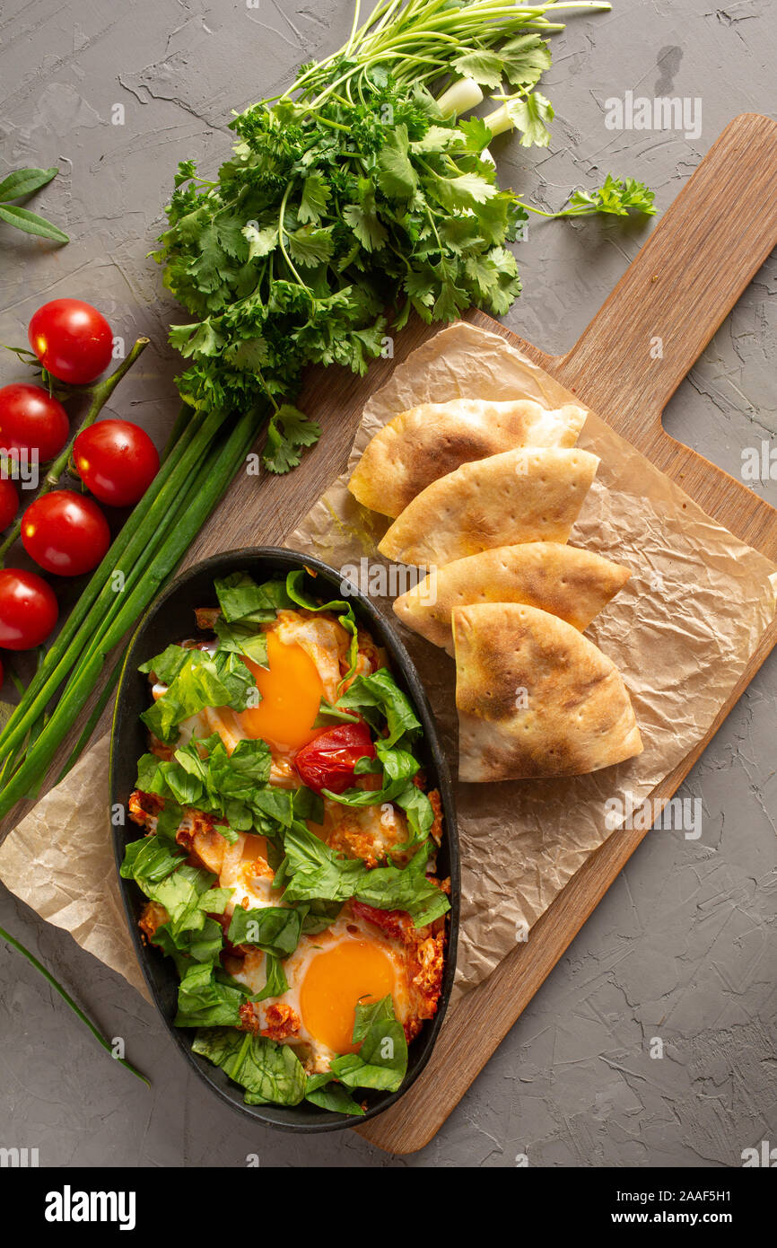 Spiegeleier mit Tomaten und Kräutern, die in einem Oval schwarz Teller auf einem Holzbrett mit Stück Kuchen Stockfoto