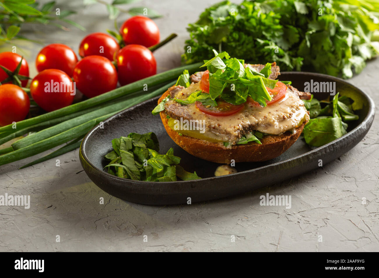 Bruschetta mit Roastbeef - gebackenes Kalbsfilet mit gesalzene Gurken, Tomaten, Spinat und Senfsauce auf einem warmen gebratene Brötchen in eine schwarze Platte auf einem g Stockfoto