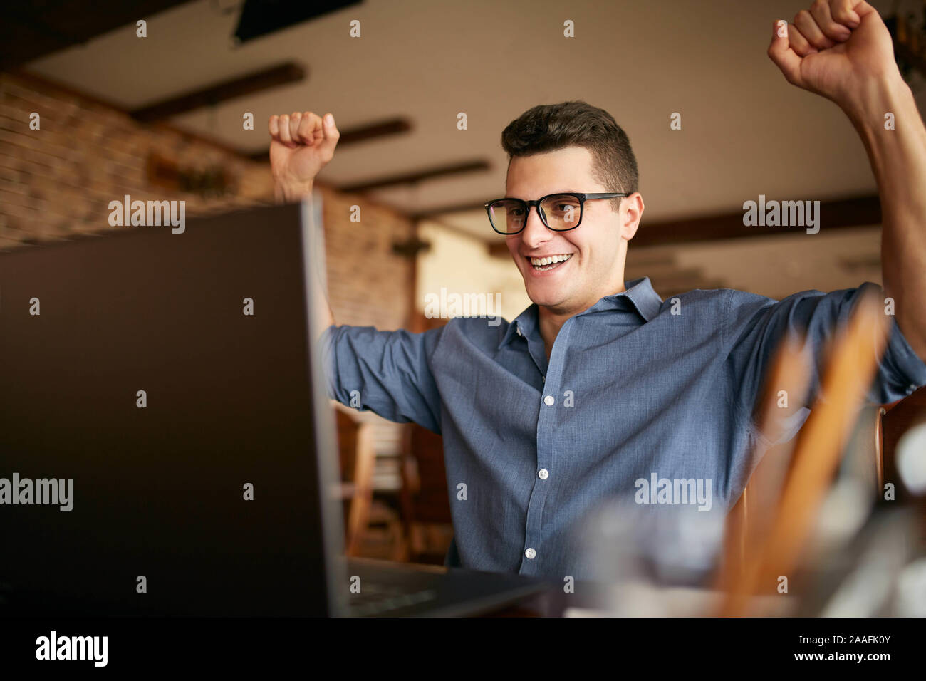 Gut aussehender Geschäftsmann mit Laptop in seine Arme mit Fäusten, Erfolge feiern. Gerne freelancer Hipster in Gläsern fertige Arbeit am Projekt Stockfoto