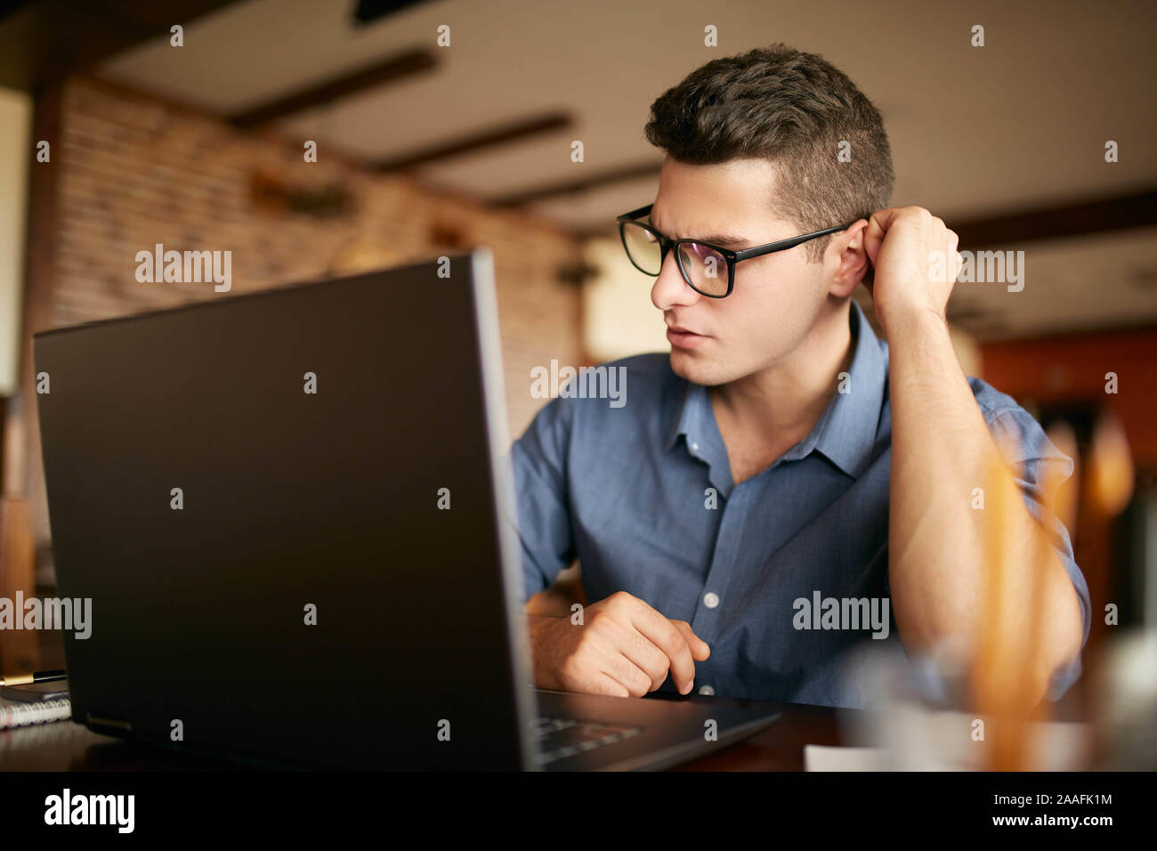 Nachdenklichen jungen kaukasischen Geschäftsmann in Gläsern Arbeiten am Laptop. Der nachdenkliche attraktive hipster Freiberufler scratch einen Kopf und denkt über Stockfoto