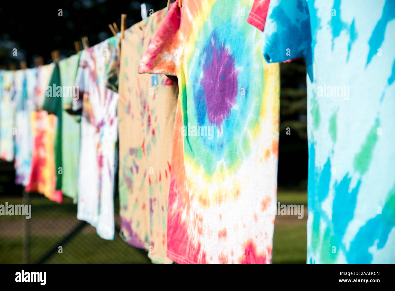 Eine Reihe von bunten Tie-dye T-Shirts hängen draußen auf einer Wäscheleine in der Sonne Stockfoto