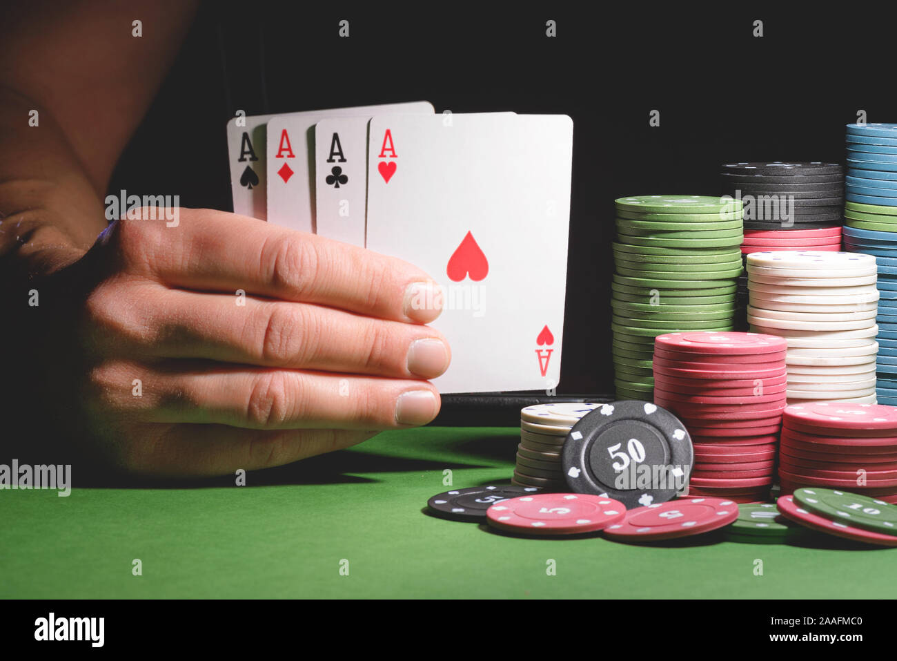 Männliche Hand mit vier Assen Karten und Poker Chips auf dem grünen Tisch Hintergrund. Stockfoto