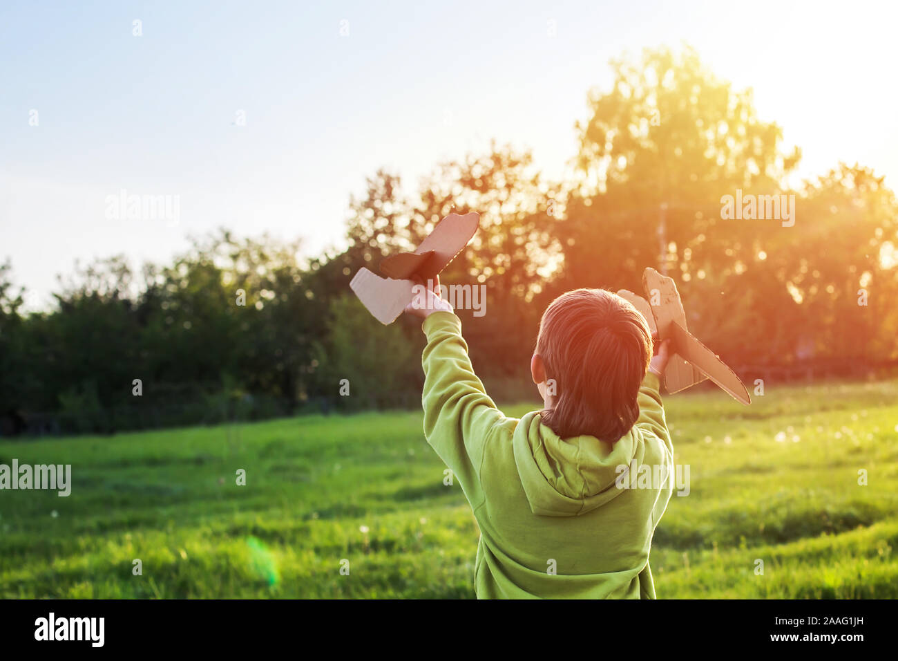 Kind startet Papierflieger. Junge, grüne Jacke über Feld bei Sonnenuntergang läuft. Glückliche Kindheit. Zu Fuß auf der Straße ohne ein Telefon. Stockfoto