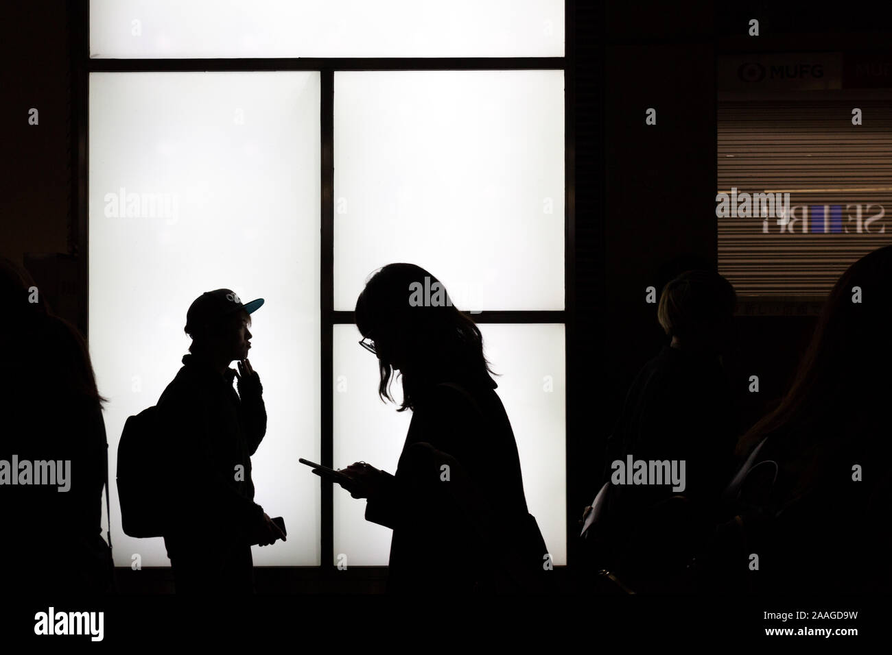 Die junge Japanerin benutzt ein Smartphone, während sie durch Menschenmengen an einer beleuchteten Wand in Shibuya, Tokio, Japan, vorbeigeht. Stockfoto