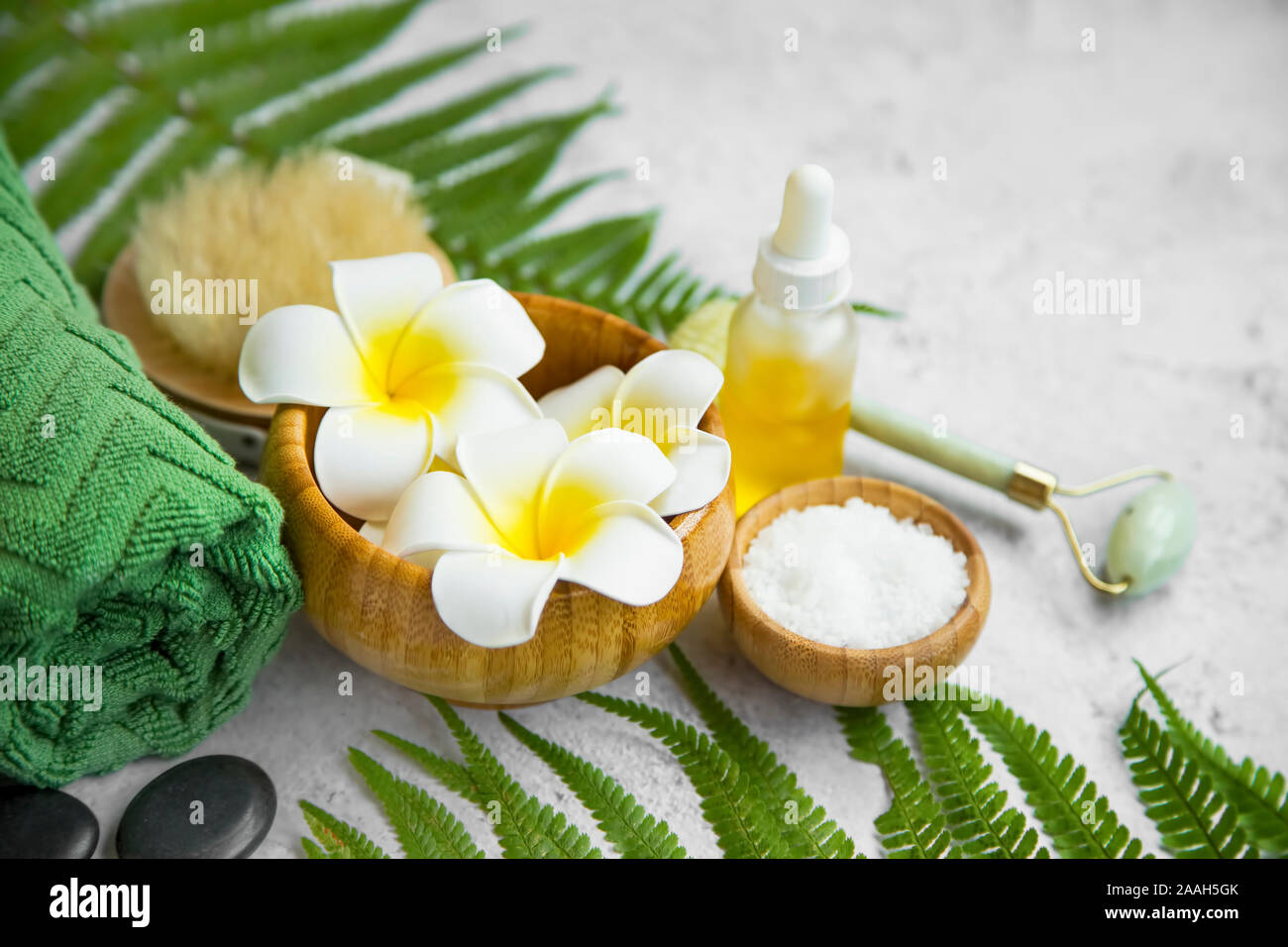 Spa Noch leben Einstellung mit Frangipani Blüten, Öl Flasche, Badesalz, Massage Steine, Handtuch und grüne Blätter, Wellness und Spa Einstellung Stockfoto
