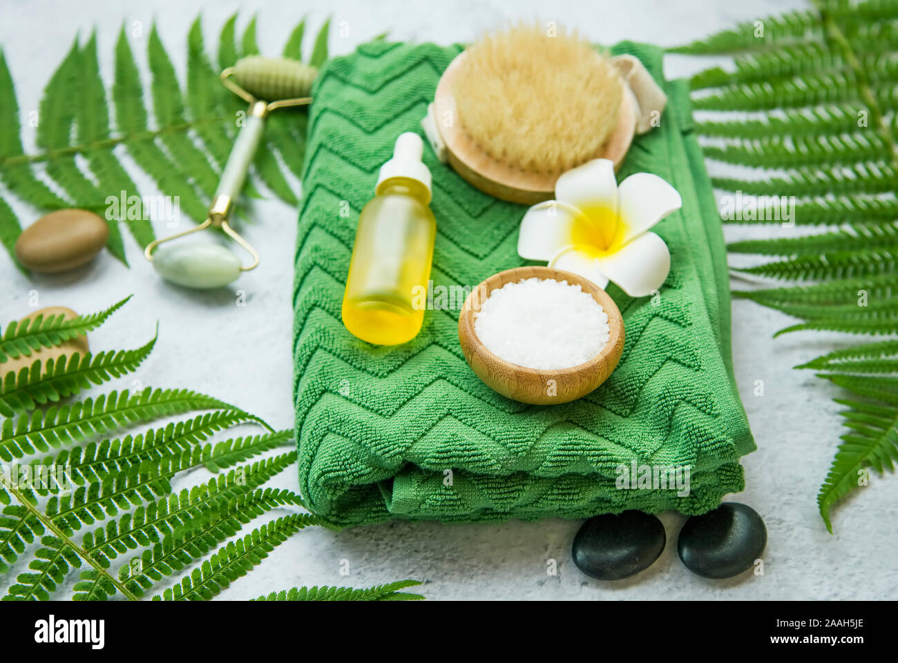 Spa Noch leben Einstellung mit Frangipani Blume, Körper Pinsel, Öl Flasche, Badesalz, Handtuch, Massage Steine und grüne Blätter, Wellness und Spa Einstellung Stockfoto