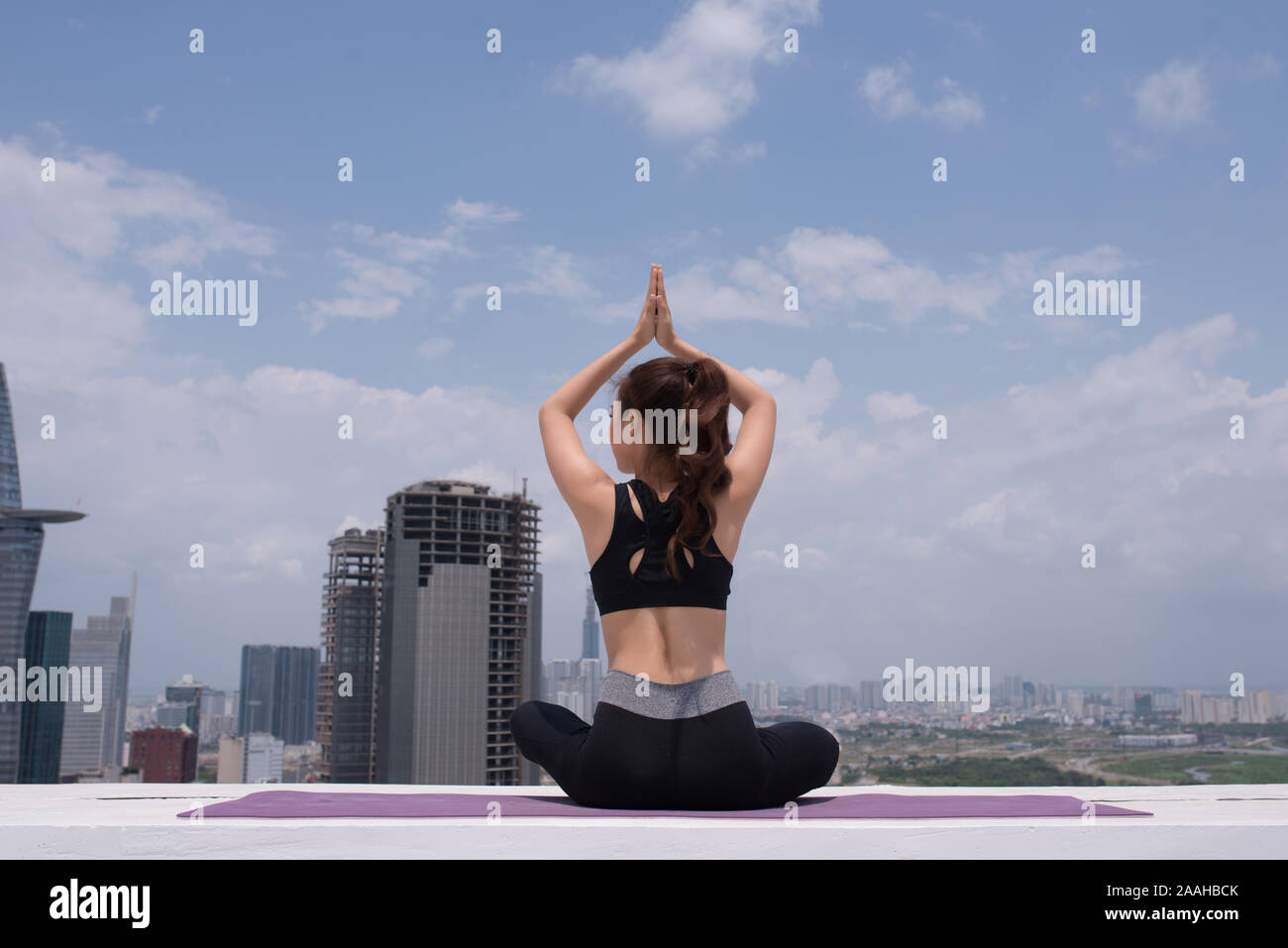 Ruhige junge Sportlerin im aktiven tragen sitzen in Pose während Yoga Ausbildung auf Gebäude auf dem Dach Stockfoto