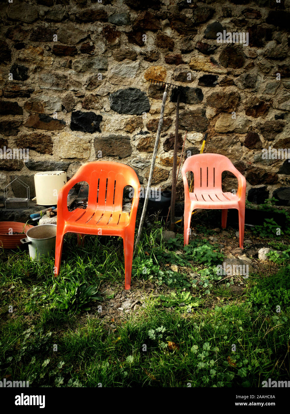 : Vertikales Bild von zwei Plastikstühlen auf dem Boden an einer Wand in einem Garten Stockfoto