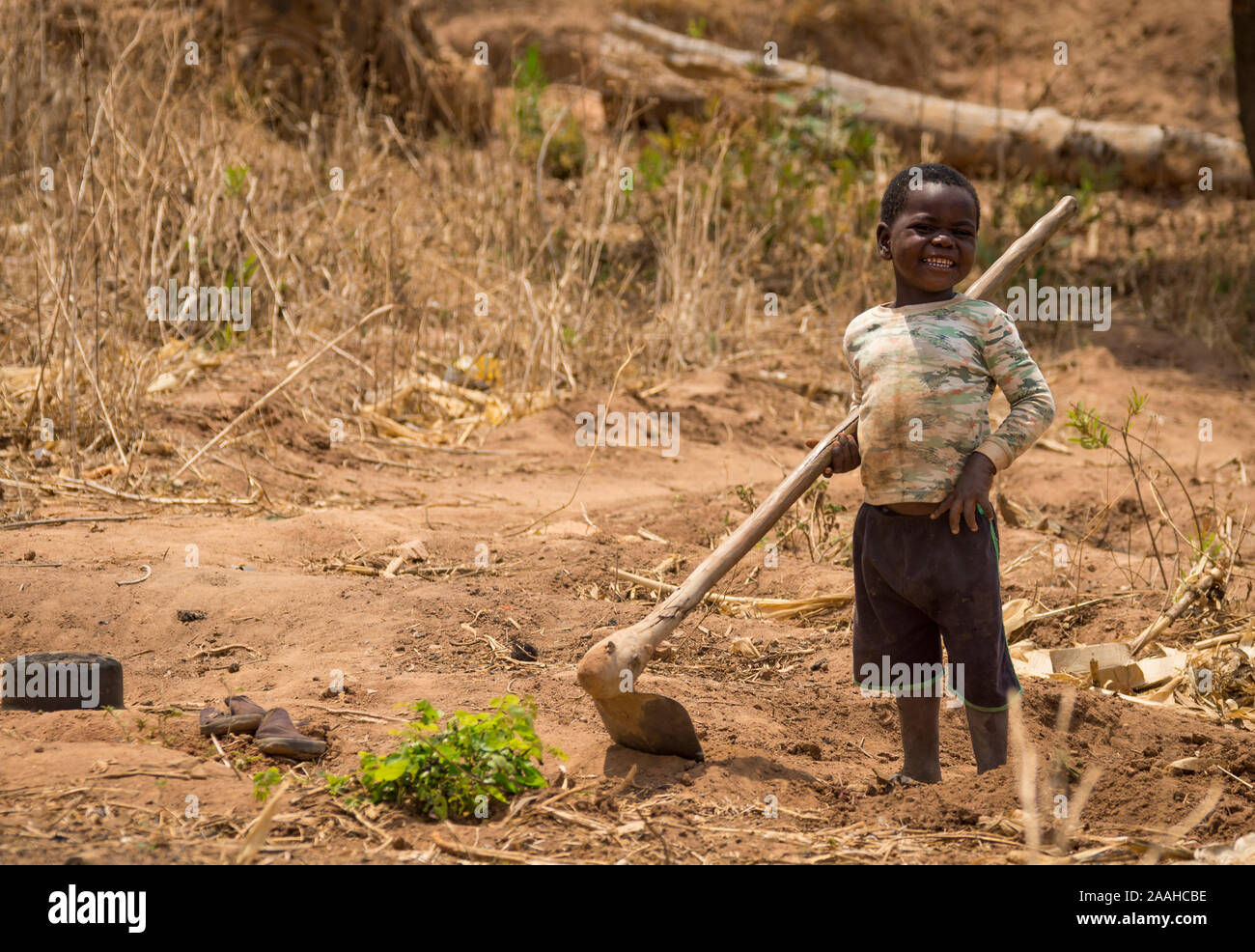 Ein junges Kind in einem ländlichen Dorf in Malawi nimmt eine Hacke Stockfoto