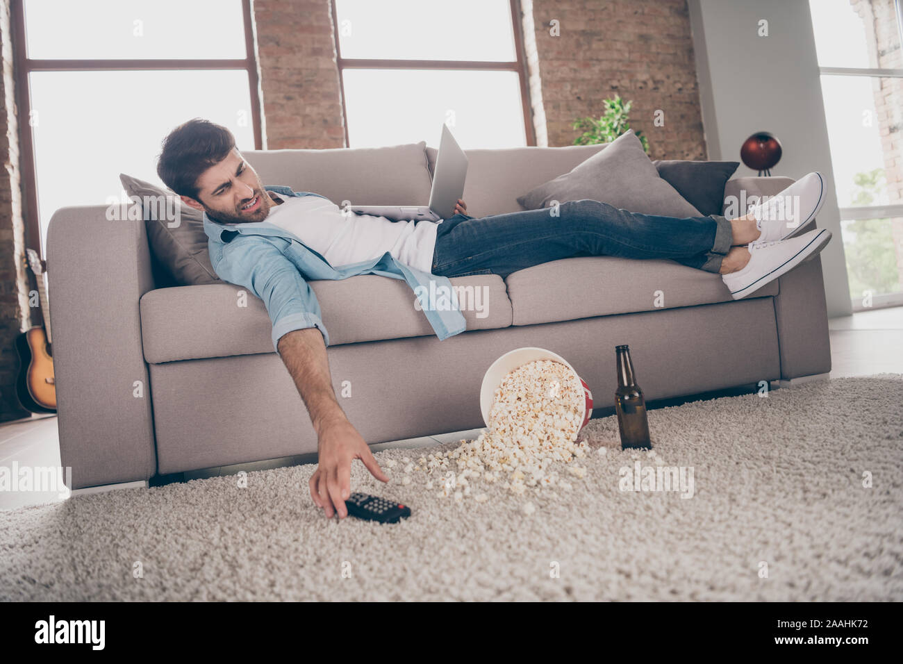 Profil Foto von Faul gemischten Rennen Kerl liegen, bequemen Sofa kann nicht TV-Fernbedienung Gerät halten Notebook nach, Fußball Hühneraugen leer Bier Stockfoto