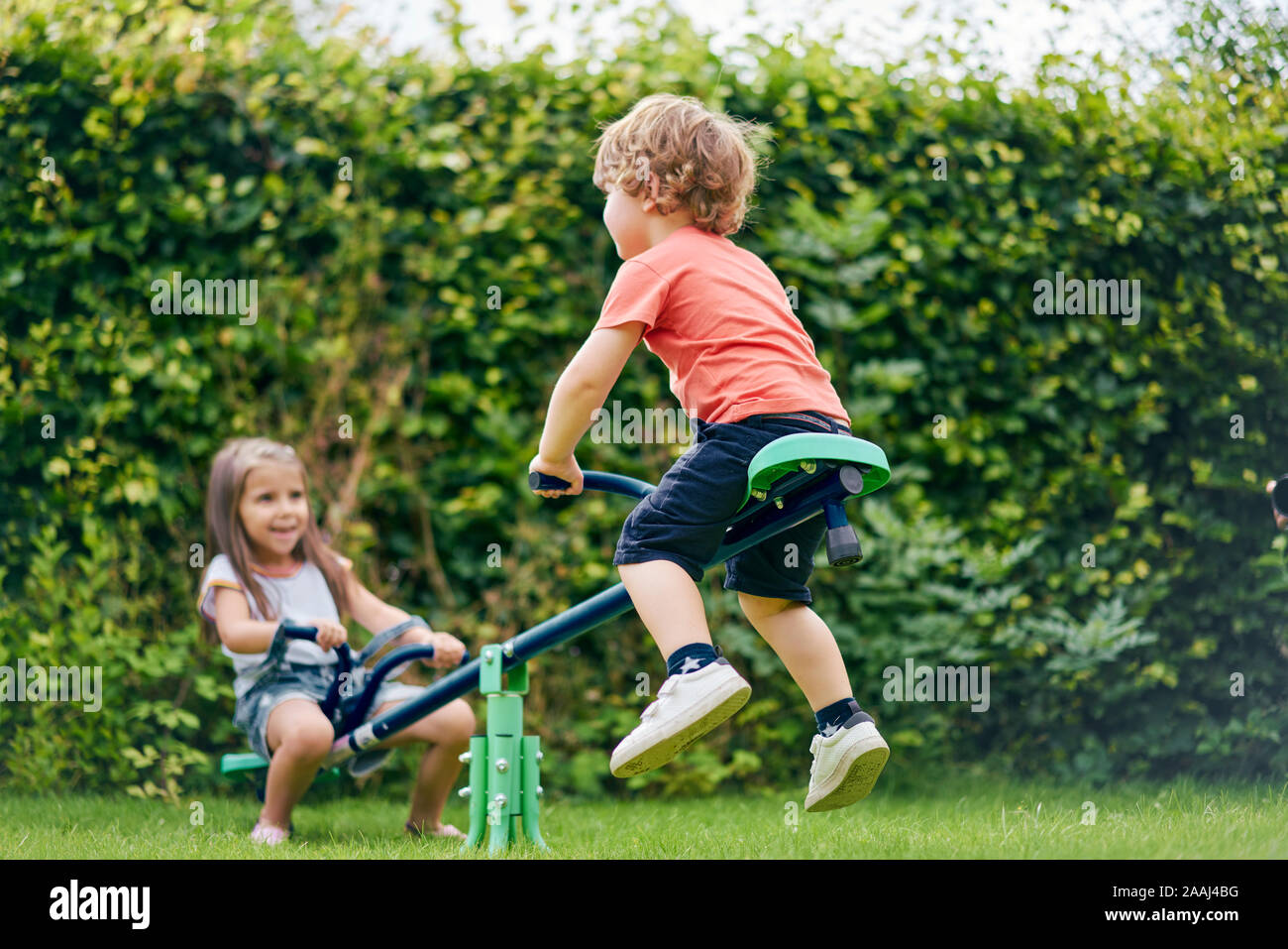 Mädchen und Jungen auf Spielzeug Schaukel im Garten Stockfoto