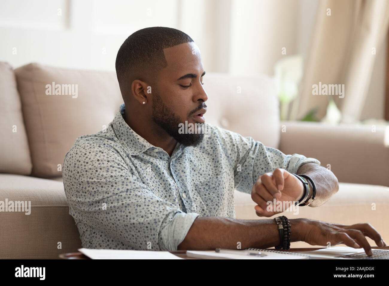 Sorgen afrikanischer amerikanischer Mann prüfen, Zeit für die Arbeit am Laptop Stockfoto