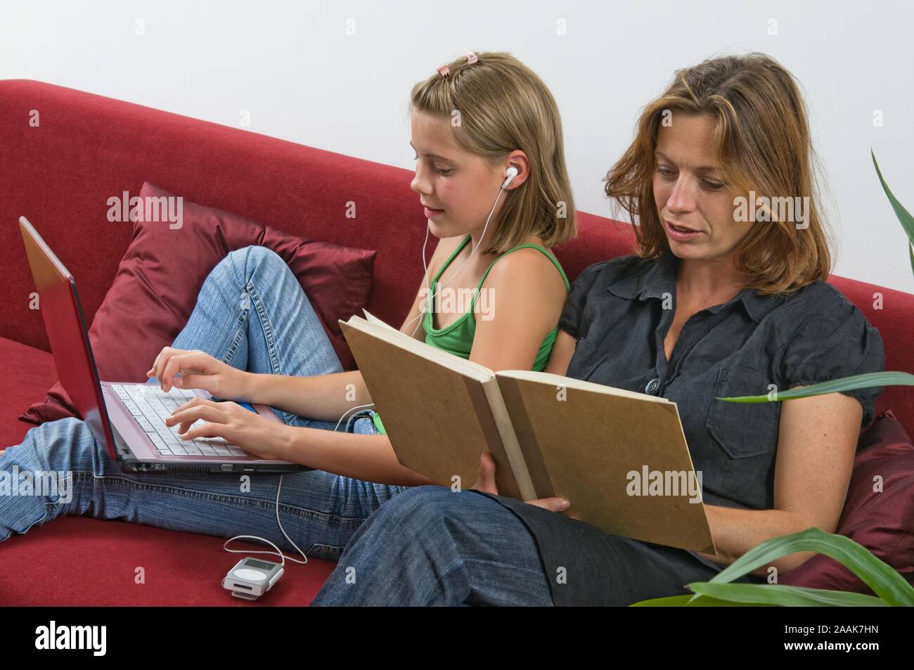 Mutter mit Buch und Tochter mit Laptop und MP3-Player auf der Couch - Mutter mit Buch und Tochter mit Laptop und MP3-Player auf der Couch Stockfoto