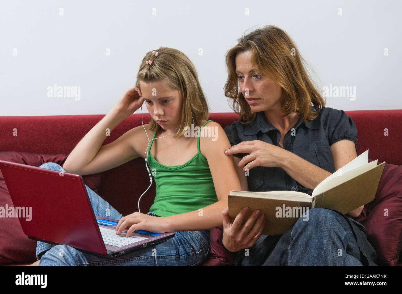 Mutter mit Buch und Tochter mit Laptop und MP3-Player auf der Couch - Mutter mit Buch und Tochter mit Laptop und MP3-Player auf der Couch Stockfoto