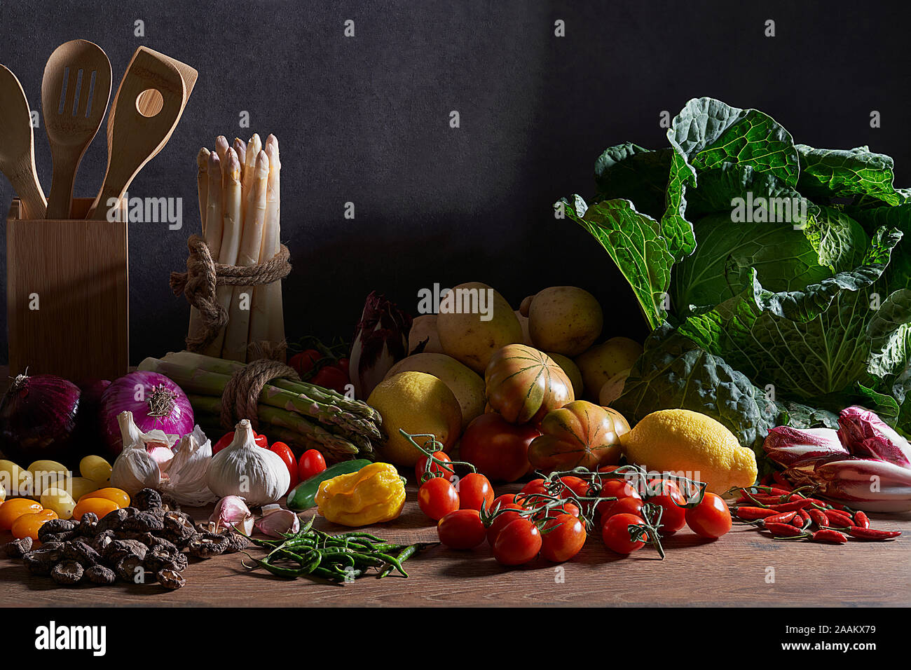 Vorderansicht von frischem Gemüse, Kohl, Tomaten, weißen und grünen Spargel, Paprika, Kartoffeln, Endivien, Pilzen, Knoblauch, Zitronen und Holz- Besteck Stockfoto