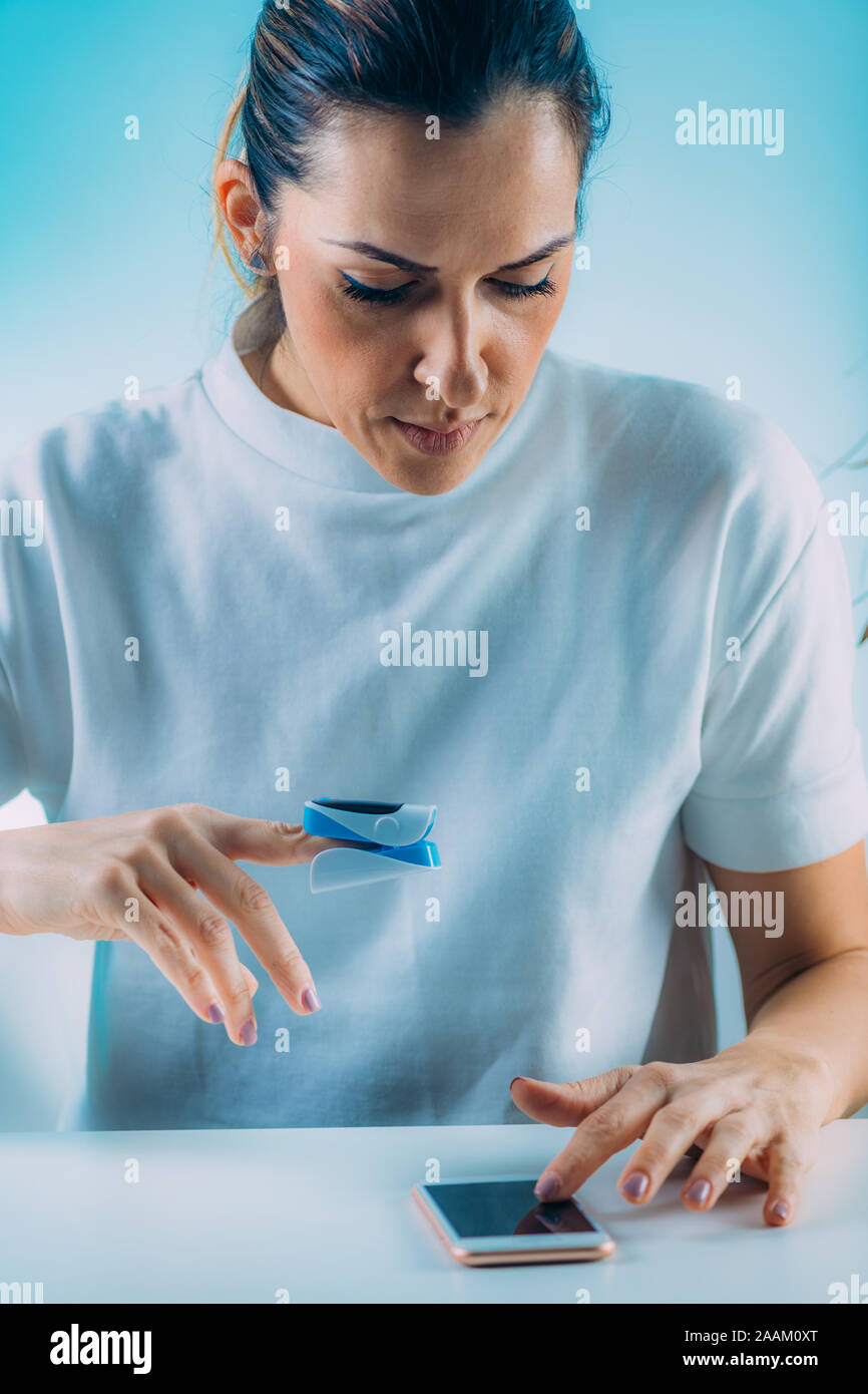 Frau mit Pulsoximeter und Smart Phone, Messung der Sauerstoffsättigung. Stockfoto