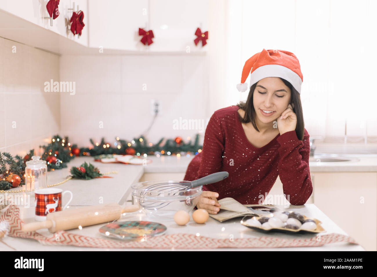 Frau liest Kochbuch in der Küche mit Weihnachtsbeleuchtung und Girlanden Stockfoto