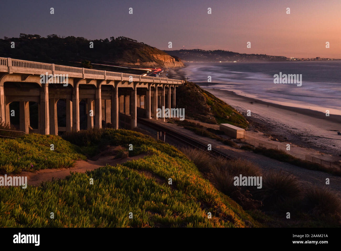 Torrey Pines Road auf der Brücke, Eisenbahnschienen unter, neben Sandstrand mit Wellen am Ufer bei Sonnenuntergang brechen, La Jolla, Kalifornien, USA Stockfoto