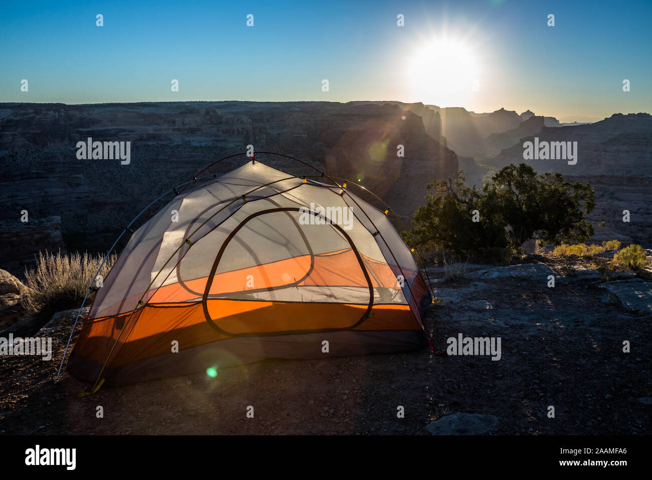 Aufwachen mit Sonnenaufgang über Campingplatz mit orange Zelt in der Nähe der Kante einer großen Schlucht in das San Rafael Swell Wüste in Utah Stockfoto