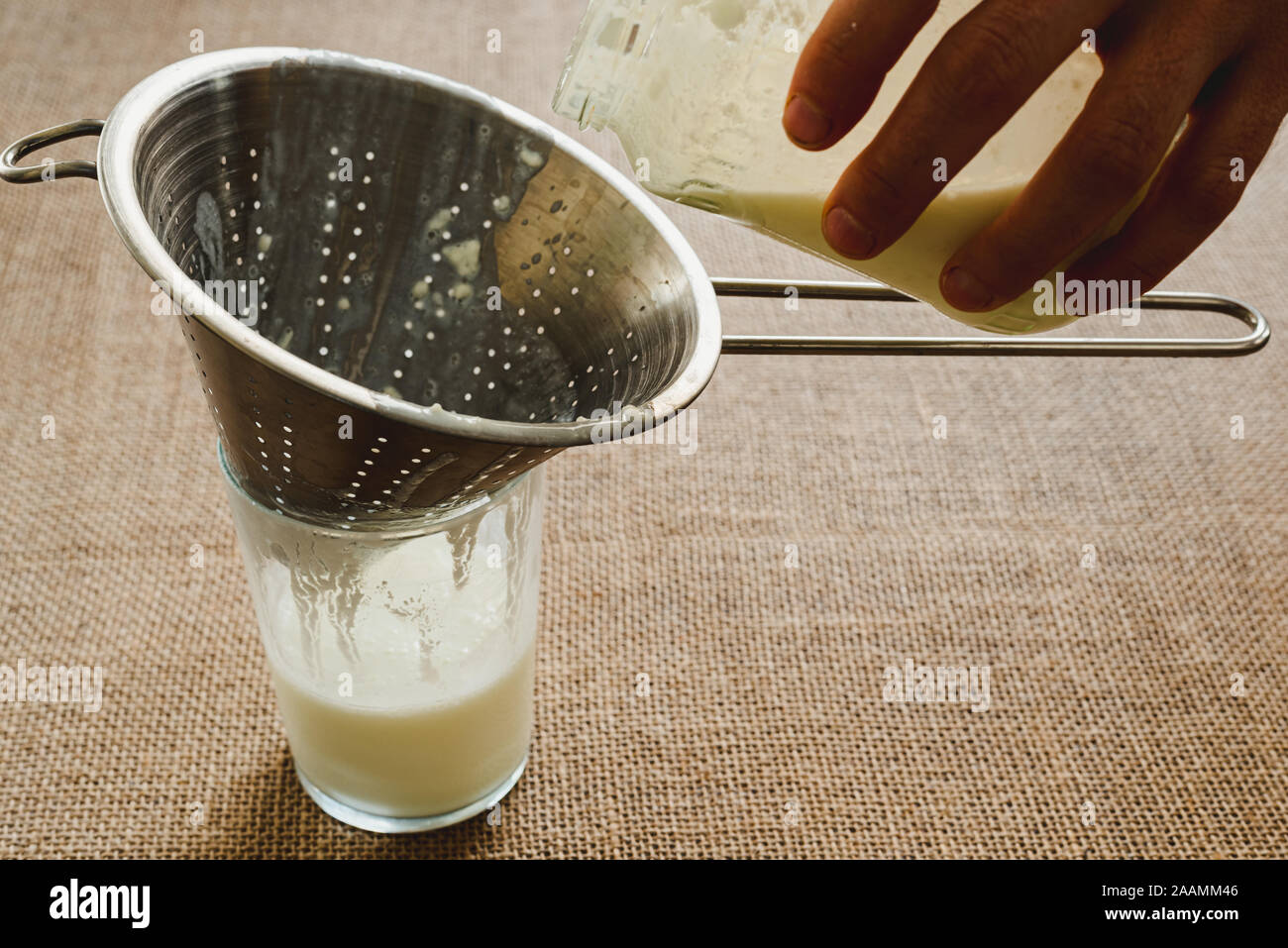 Die Hand des Mannes gießt Milch Kefir in eine Kanne ein gesundes Frühstück für die intestinale Mikrobiota vorzubereiten. Stockfoto