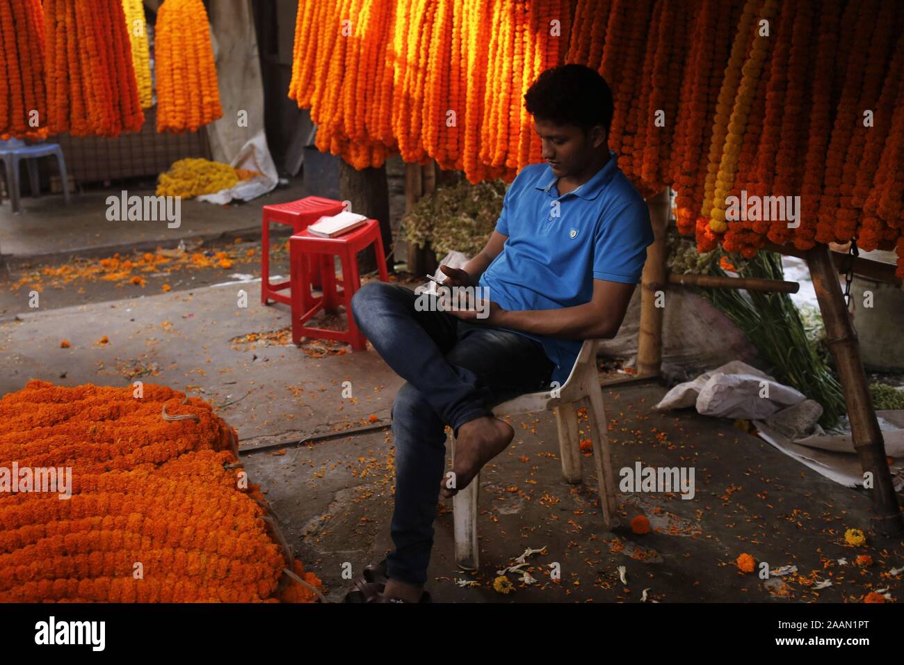 Dhaka, Bangladesch. 23 Nov, 2019. Ein Anbieter nutzt sein Handy, als er für die Kunden in einem Großhandel Blumenmarkt in Dhaka wartet. Heute ist die Nachfrage nach Blumen ist gesunken, da viele Unternehmen künstliche Blume herstellen. Credit: MD Mehedi Hasan/ZUMA Draht/Alamy leben Nachrichten Stockfoto