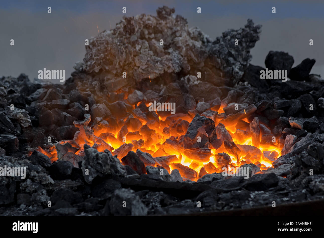 Bügeleisen bar Glühen in tragbaren Forge brazier. Itglieder Leuchten in einer Schmiede. Feuer, Hitze, Kohle, Asche mit Funkenflug im Dunkeln. Feuer, Hitze, Kohle, Asche mit Stockfoto