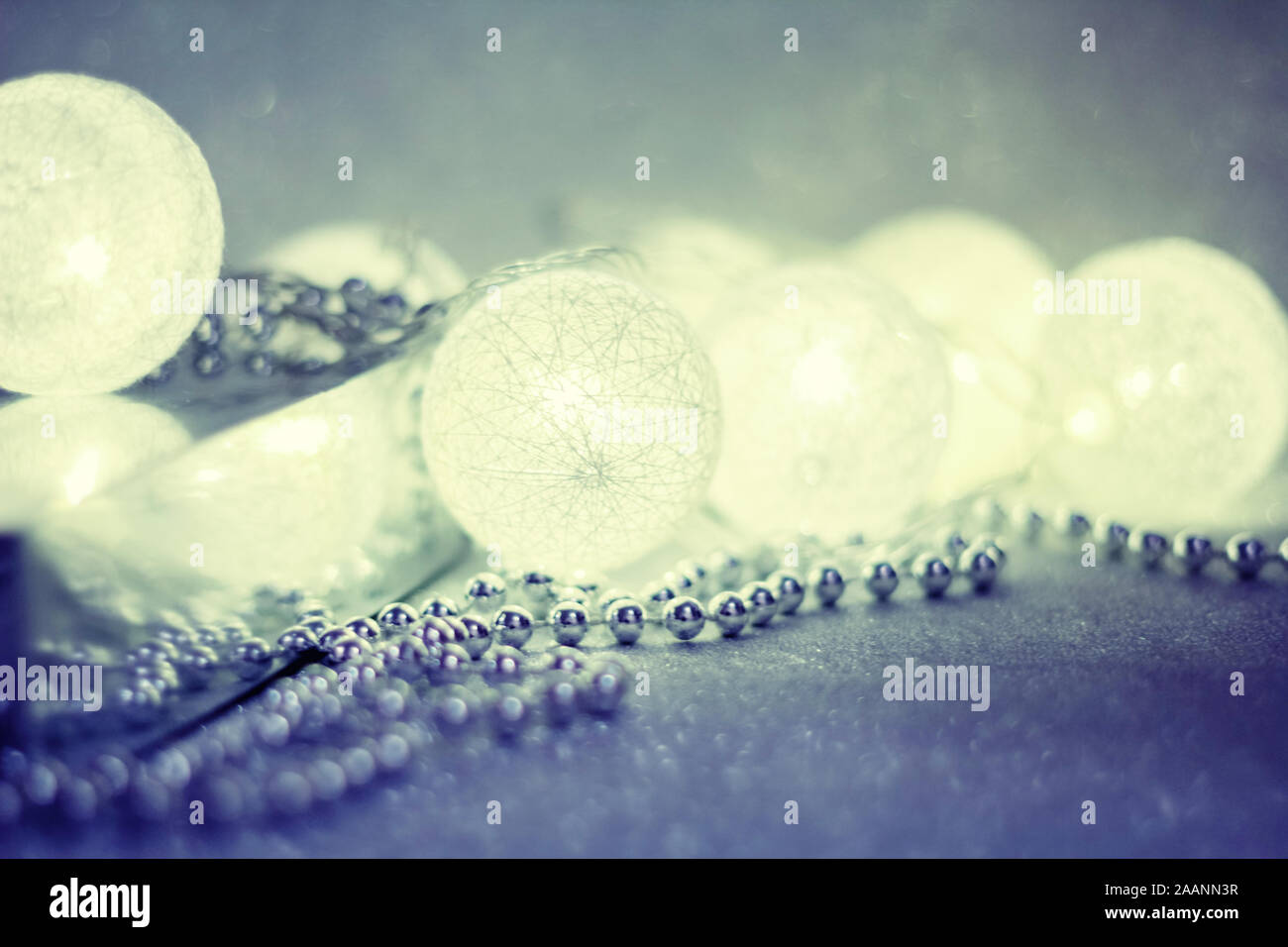 Helle Girlande in Form von Kugeln leuchtet auf einem silbernen funkelnden Hintergrund, neben Silberperlen, eine Kopie des Raumes für Ihr Design. Frohe Weihnachten Stockfoto