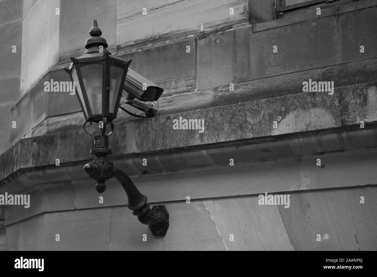 Überwachungskameras (CCTV) hinter einem alten viktorianischen Stil Straßenlaterne an der Seite eines historischen Gebäudes mit einem architektonischen Gesims entfernt Stockfoto