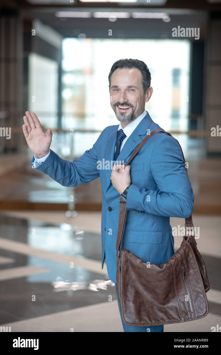 Bärtige Geschäftsmann mit braunem Leder Tasche winkende Hand beim Ausscheiden aus dem Amt Stockfoto