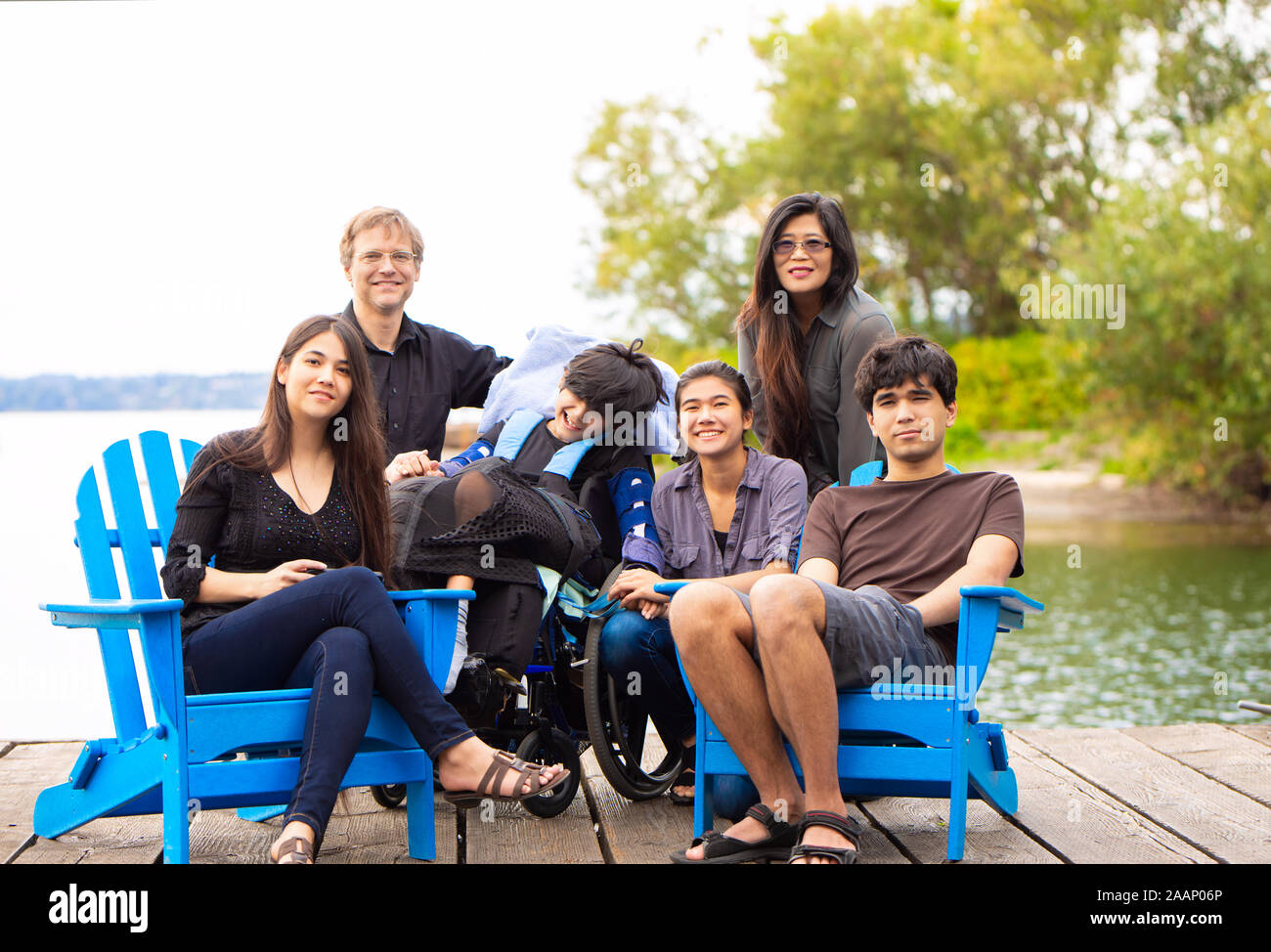Multirassischen Familie mit besonderen Bedürfnissen Kind sitzen im Freien zusammen auf Sommertag. Kind sitzt im Rollstuhl. Stockfoto