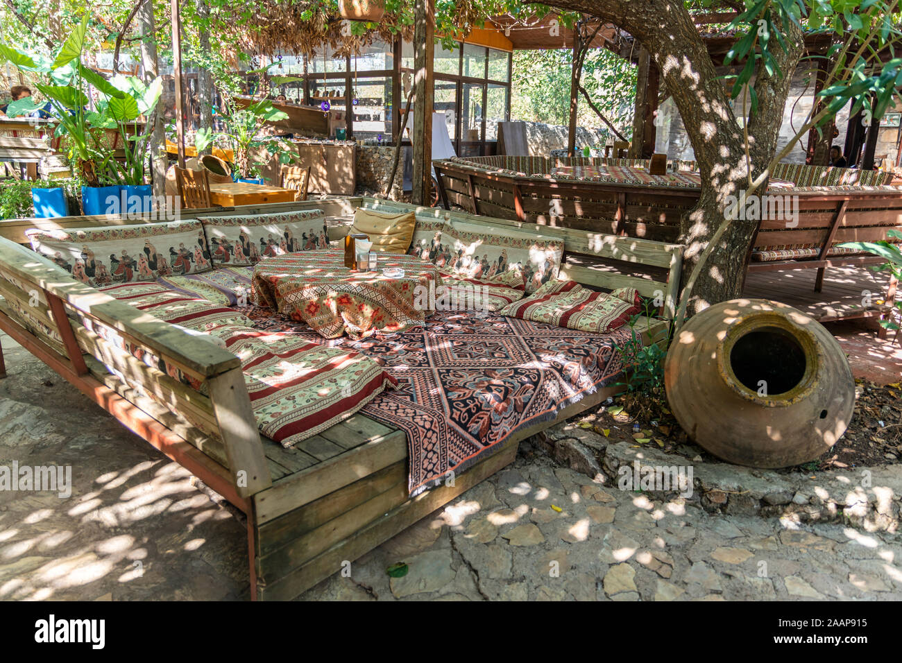 Erhöhte Sitzbereich mit Teppichen und Kissen auf ein türkisches Restaurant in dappled Schatten eines Garten im Freien. Stockfoto