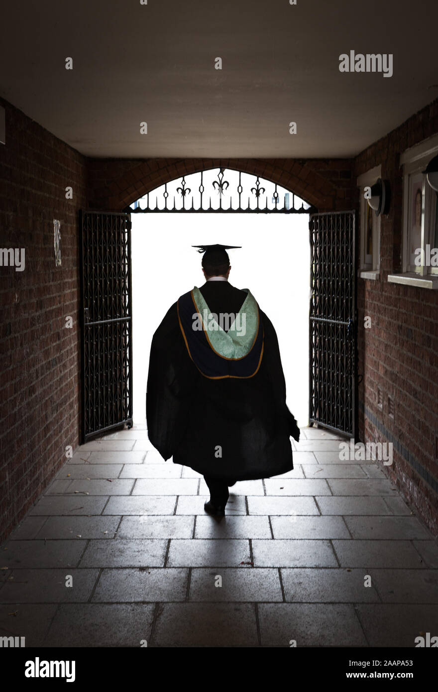 Eine Rückansicht eines Universitätsabsolventen in Vollkleid Durch den Torbogen in das Licht, das die Zukunft darstellt Stockfoto