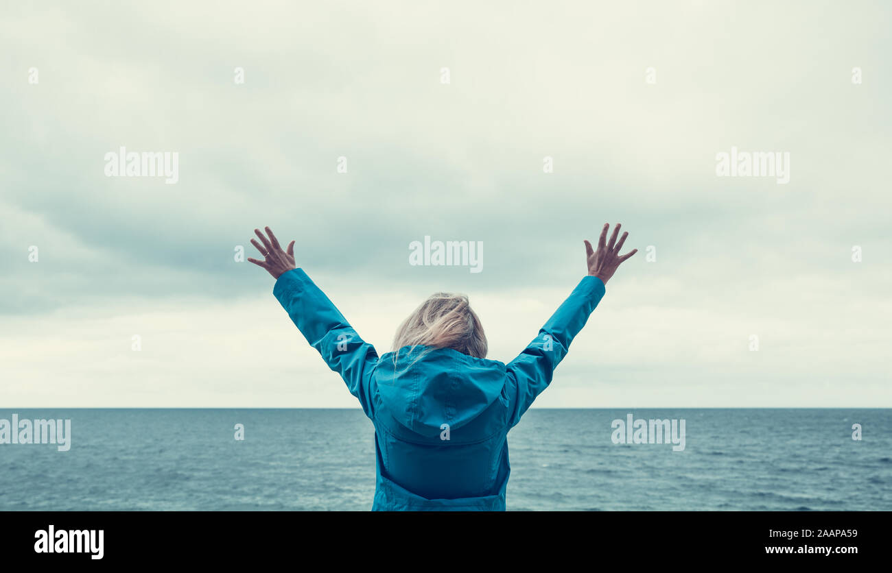 Ein Rückansicht einer Frau an einem menschenleeren Strand mit hoch in der Luft erhobenen Armen, die Freiheit, Individualität, Wohlbefinden und Freude darstellen Stockfoto