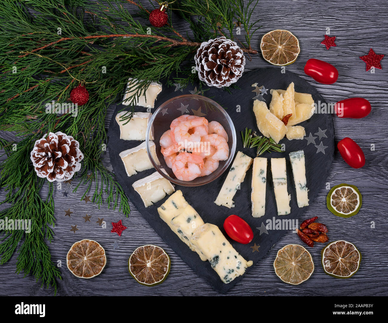 Eine dunkle Käseplatte mit Harissa und Garnelen, Parmesan, Gorgonzola, Rosmarin, Olivenöl und Kekse. Italienische Küche mit Weihnachten Dekor. Stockfoto