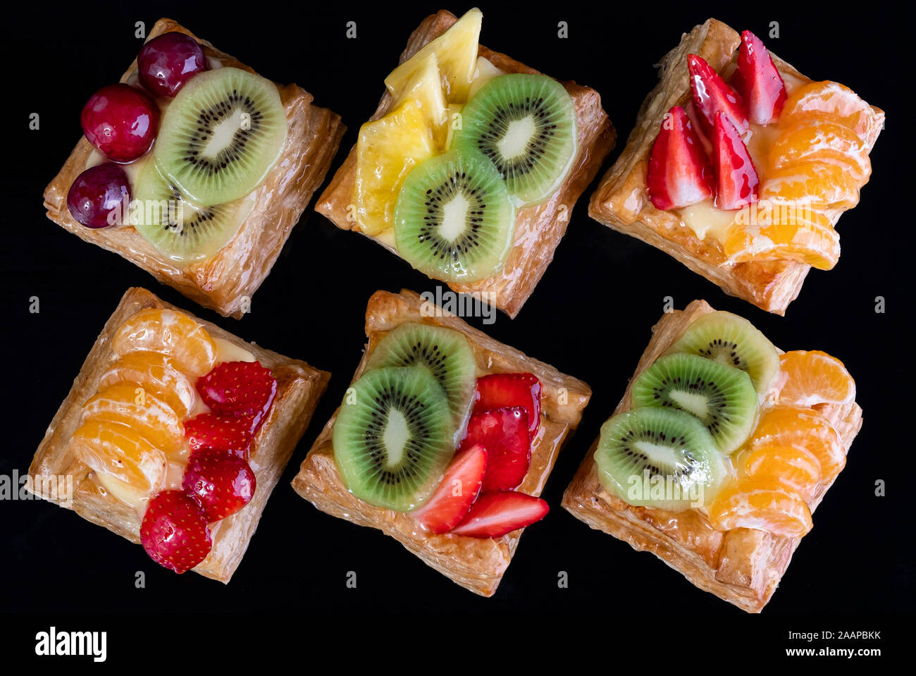 Blätterteig mit Mandarine, Kiwi und Erdbeeren Obst auf schwarzem Hintergrund gesehen von oben Stockfoto