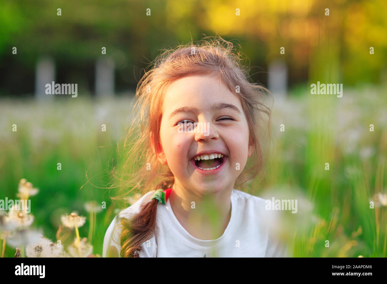 Schöne Mädchen lachen und spielen mit Blumen im sonnigen Frühling Park. Happy cute kid Spaß im Freien bei Sonnenuntergang. Stockfoto
