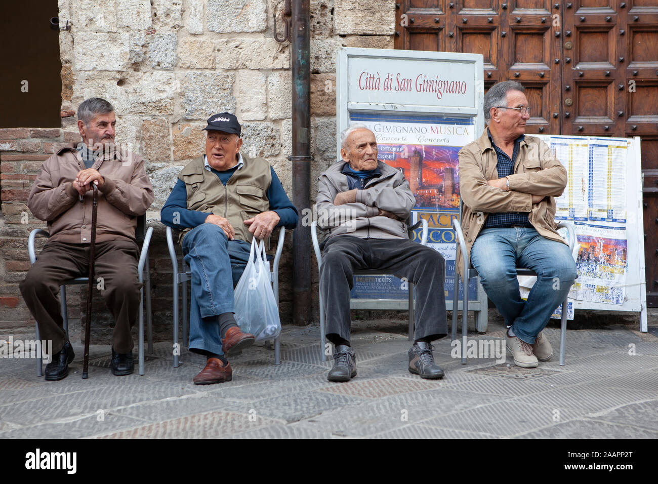 Ältere Männer sitzen zusammen auf einer Bank in San Gimignano, Toskana, Italien zu tratschen und der Welt zuzuschauen, Stockfoto