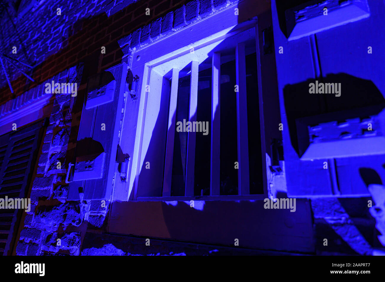 Alte Fenster mit starken Metallstangen in der Nacht blau beleuchtet Stockfoto