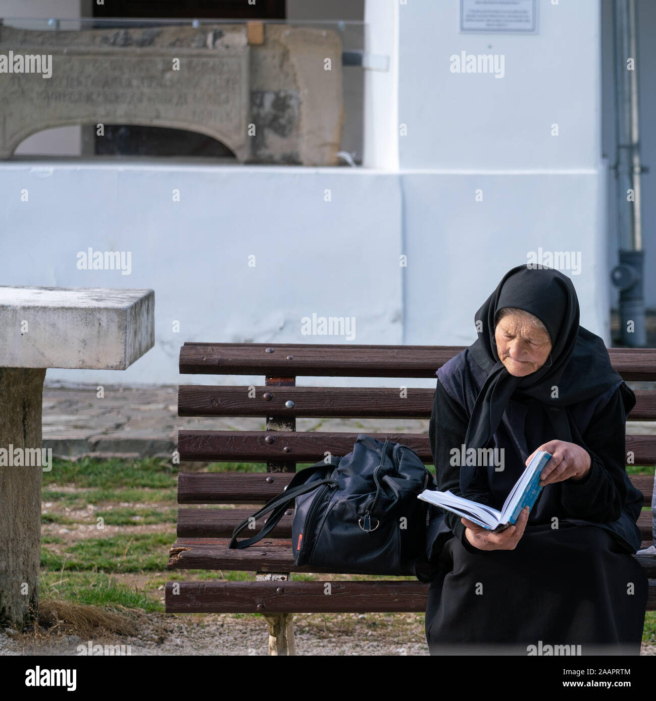Sinaia, Rumänien - November 16, 2019: Ältere religiöse Frau praktizierende Orthodoxe katholische Christentum, sitzen auf einer Bank vor der Alten Kirche Stockfoto