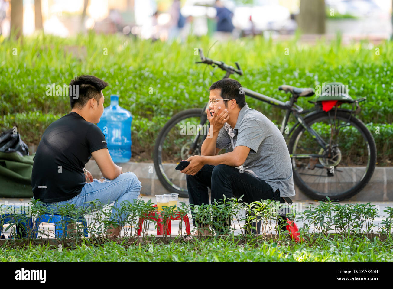 Hanoi, Vietnam - 12. Oktober 2019: Zwei junge asiatische Männer sitzen Sie in einem Park auf Plastik Schemel Saft trinken und reden über den Tag Stockfoto