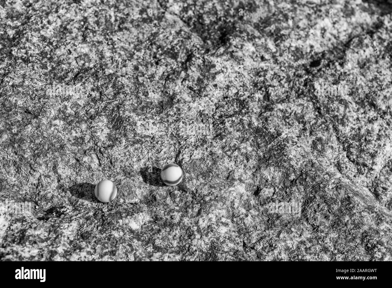 Schwarz-weiße Glasmarmeln auf rauer Steinoberfläche. Für etwas verloren, geistige Gesundheit, verlieren Ihre Murmeln, abstrakte Sphären, Träume, Biden und Murmeln. Stockfoto